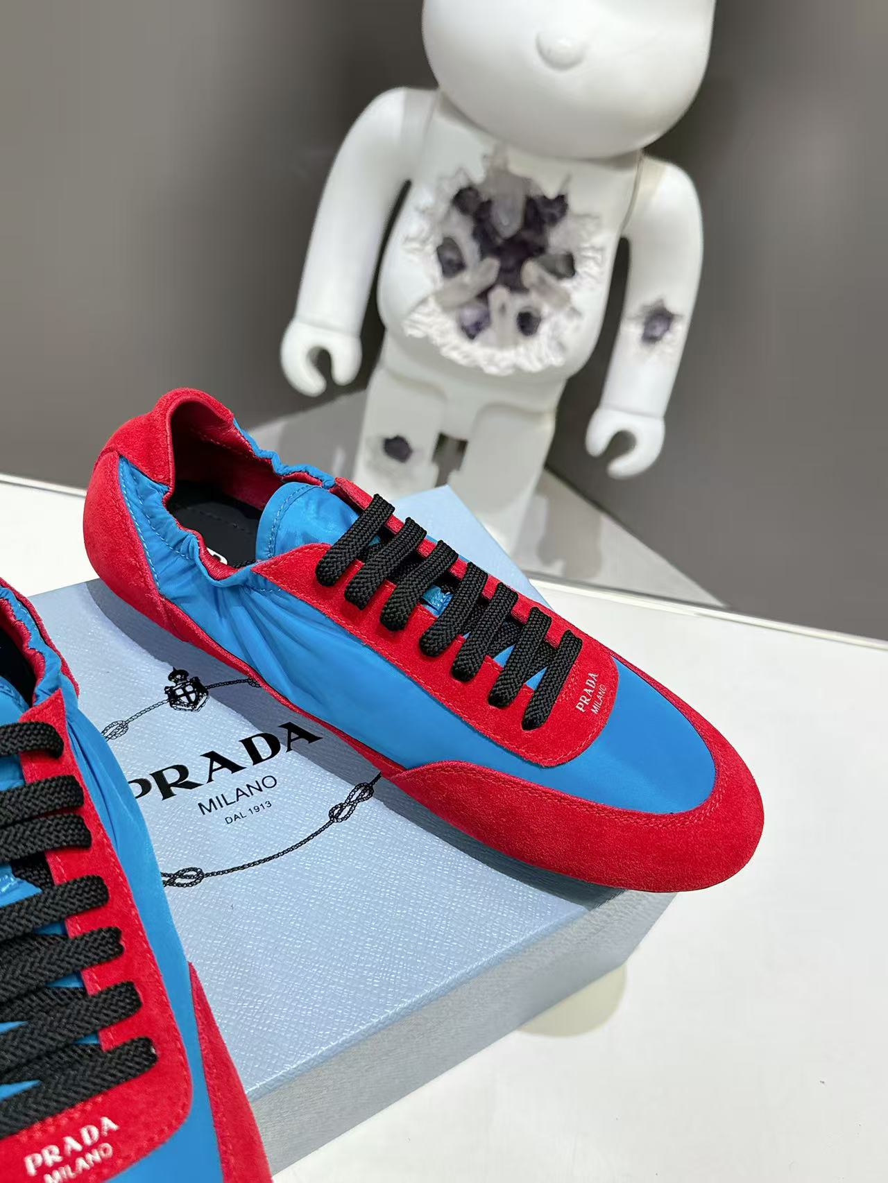 Prada unisex sneakers close-up: black laces on red and blue suede panels
