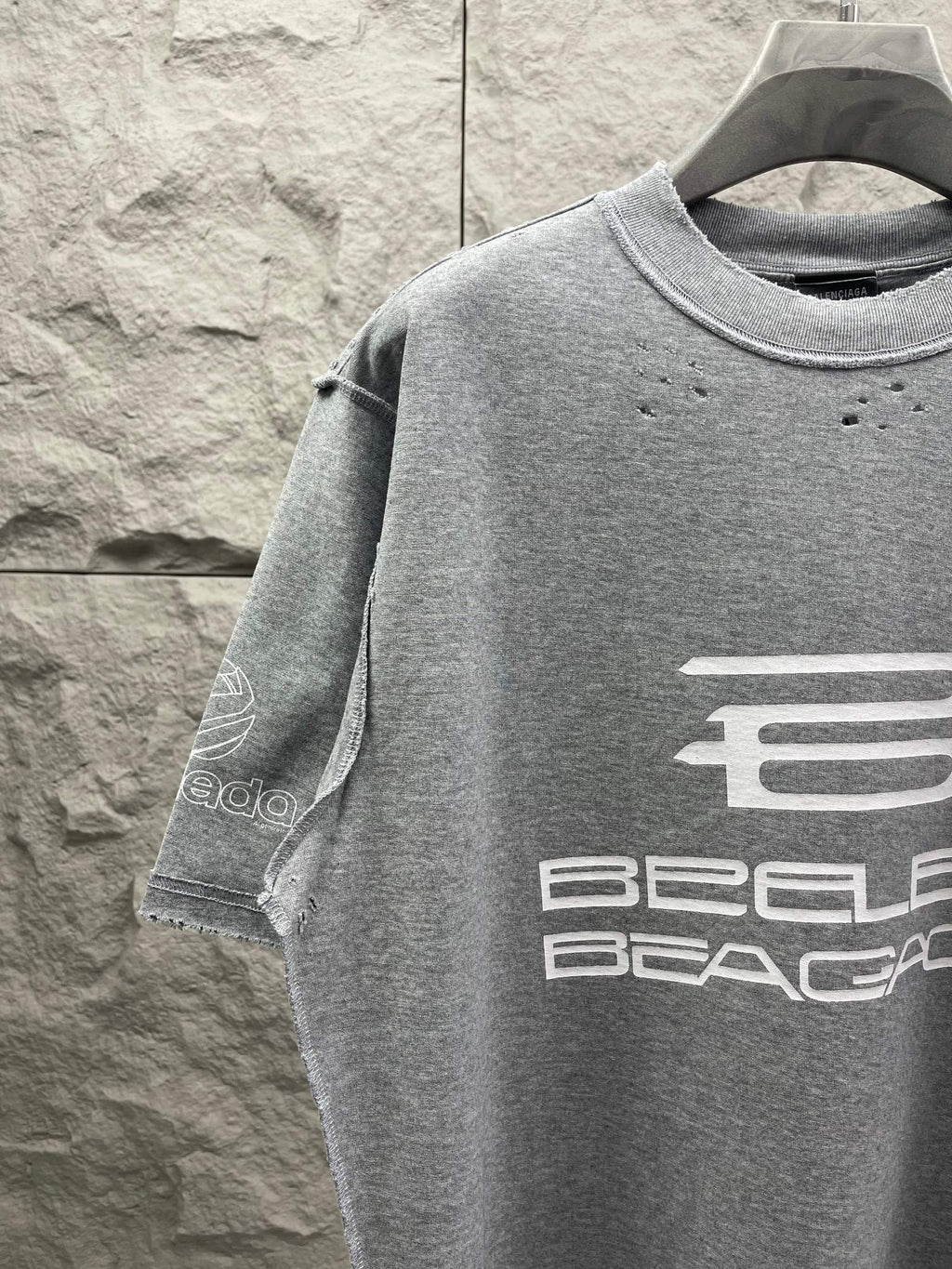 Grey T-shirt with front logo graphic and sleeve detail.