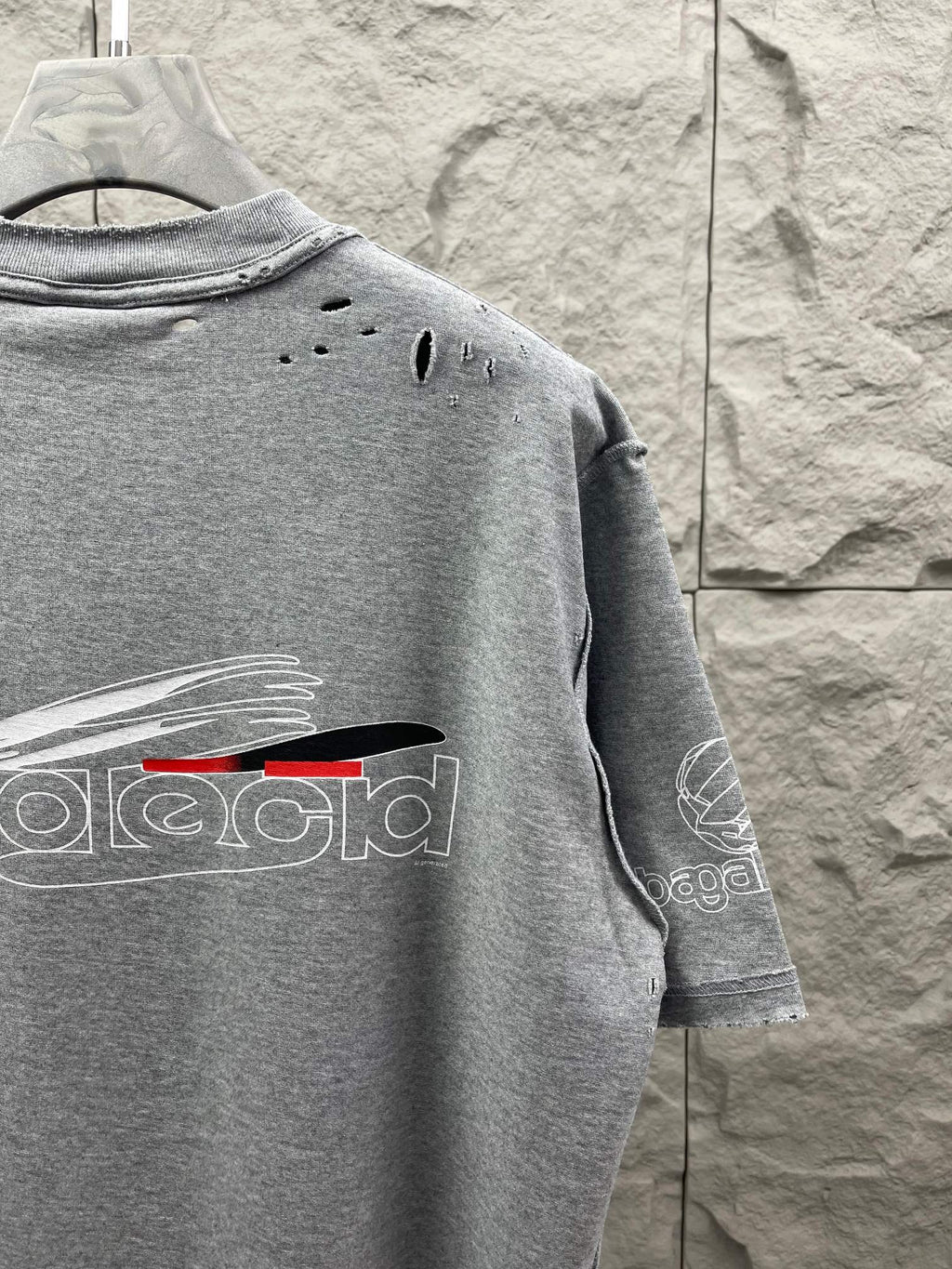 Grey T-shirt back with small distressed holes and partial logo print.