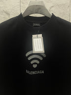 Balenciaga dark T-shirt detail: Wi‑Fi heart graphic and printed logo at center