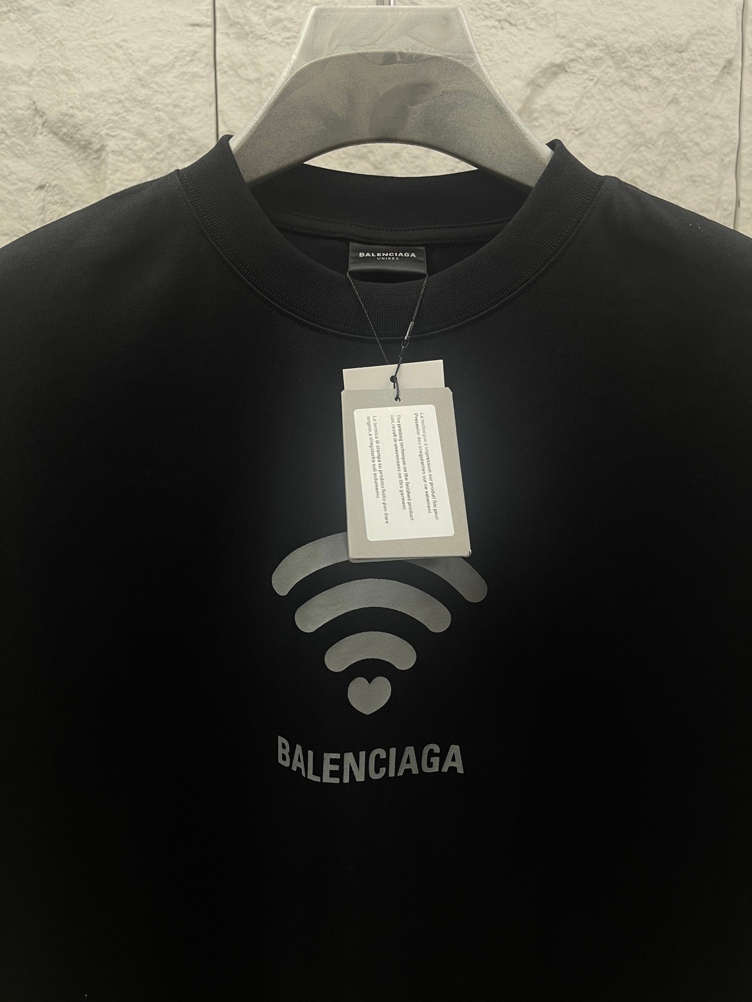 Balenciaga dark T-shirt detail: Wi‑Fi heart graphic and printed logo at center