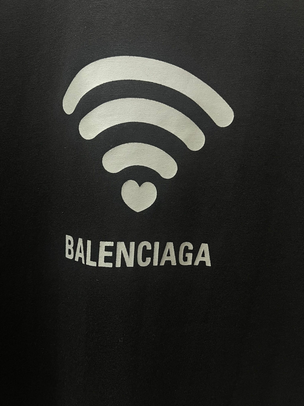 Balenciaga dark T-shirt graphic close-up: Wi‑Fi lines, heart icon, logo text