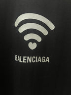Balenciaga dark T-shirt graphic close-up: Wi‑Fi lines, heart icon, logo text