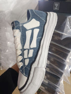 Denim low-top sneakers side view with white H-style overlays and cream laces
