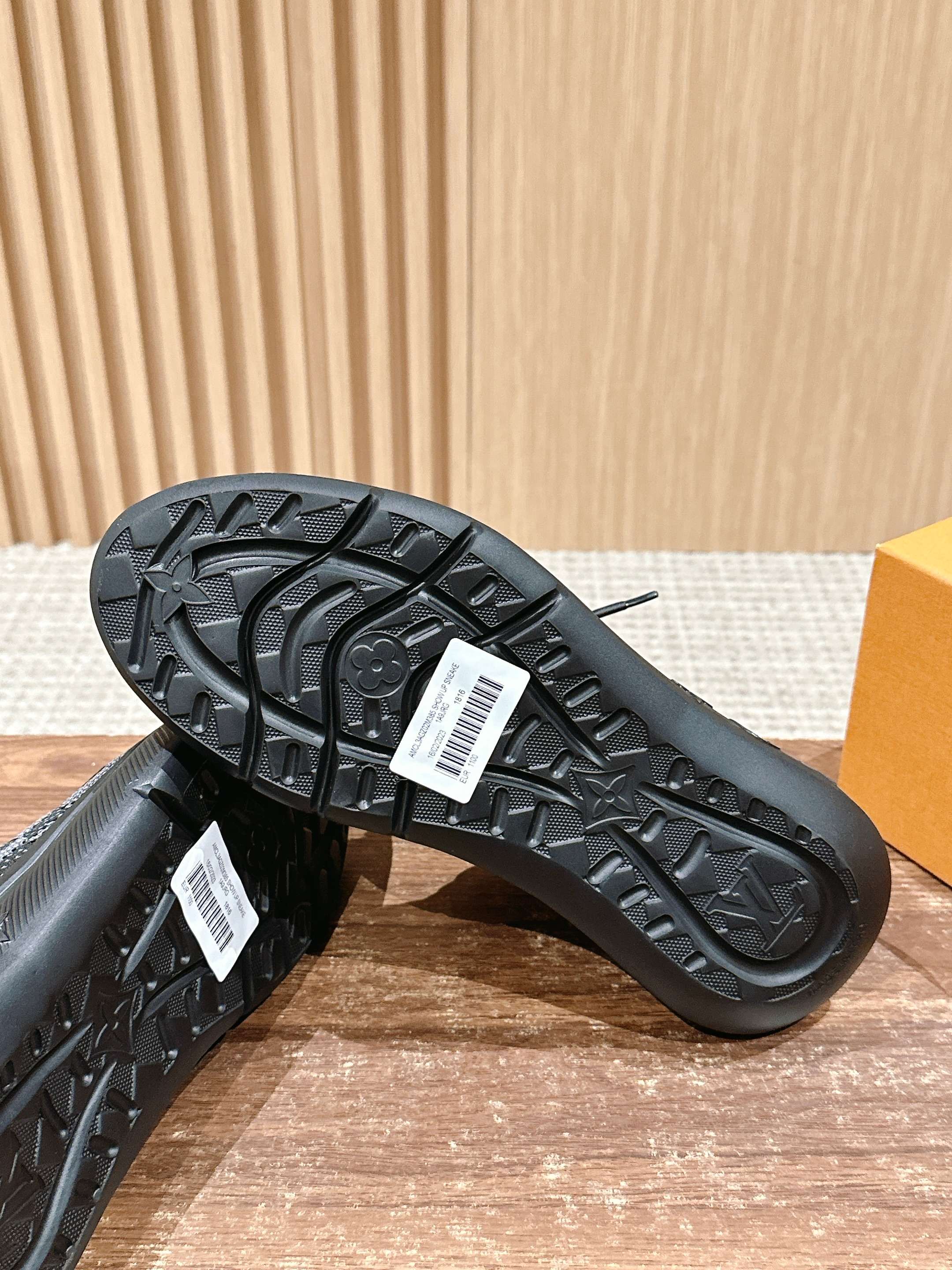 Black sneaker outsole with detailed tread pattern and logo patch near arch.