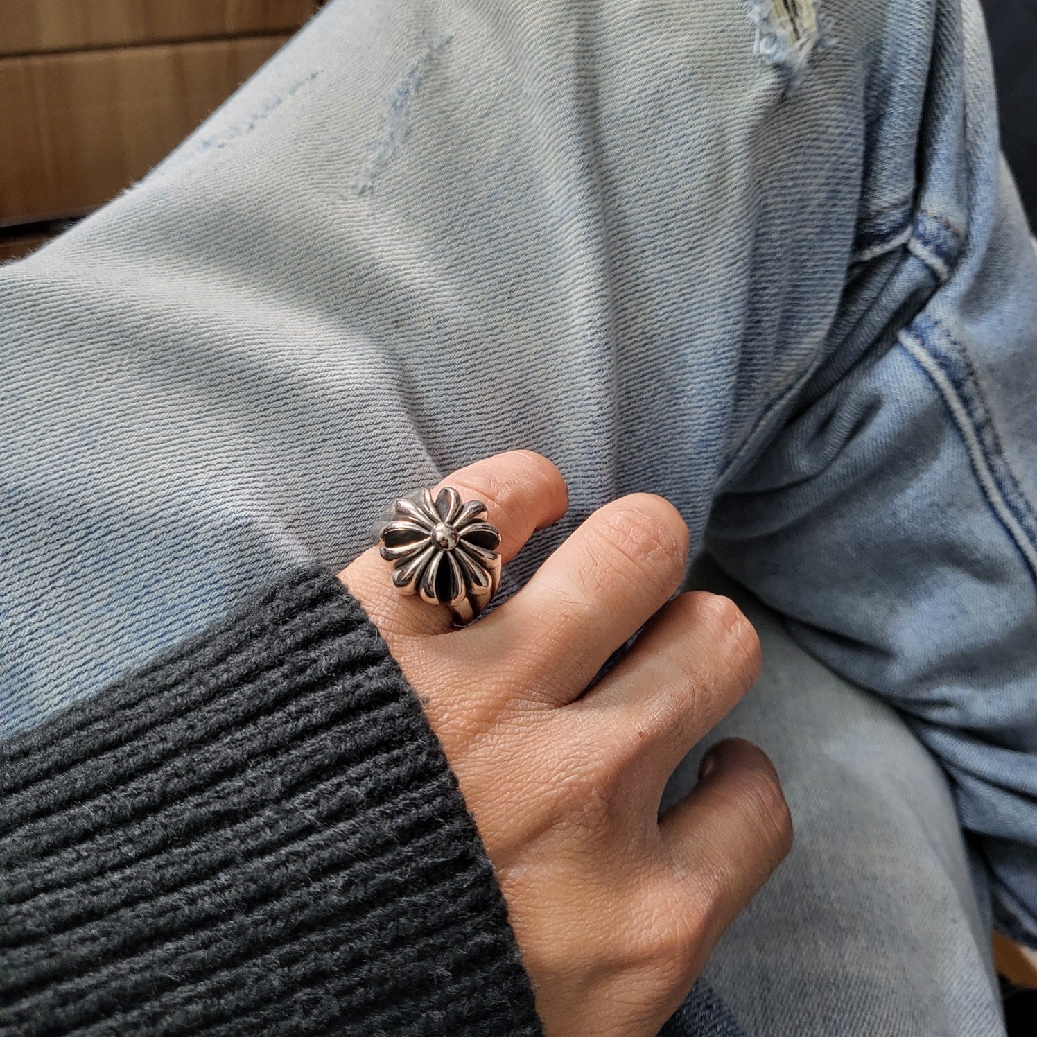 Silver-tone flower ring worn on hand with dark knit sleeve