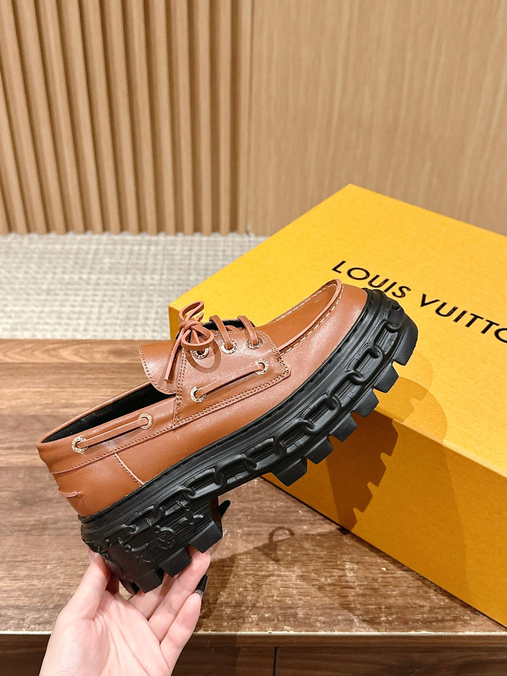 Tan leather lace-up shoe held for display, black lug sole, round toe
