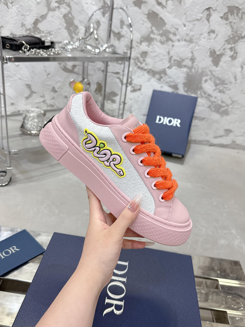 Pink and white low-top sneakers with orange laces and embroidered side logo
