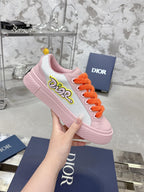 Pink and white low-top sneakers with orange laces and embroidered side logo