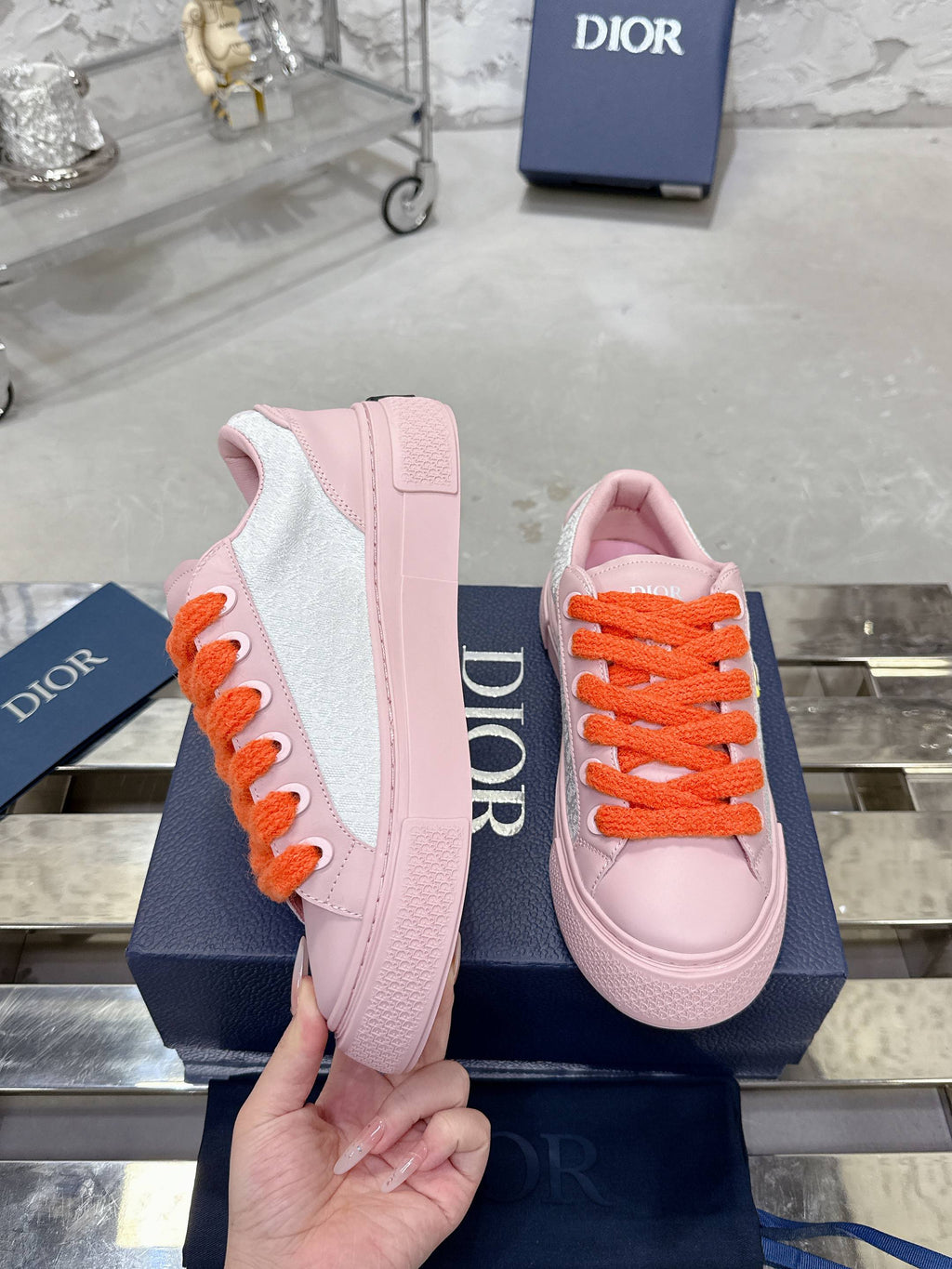 Pink and white low-top sneakers with orange laces and Dior logo on the heel