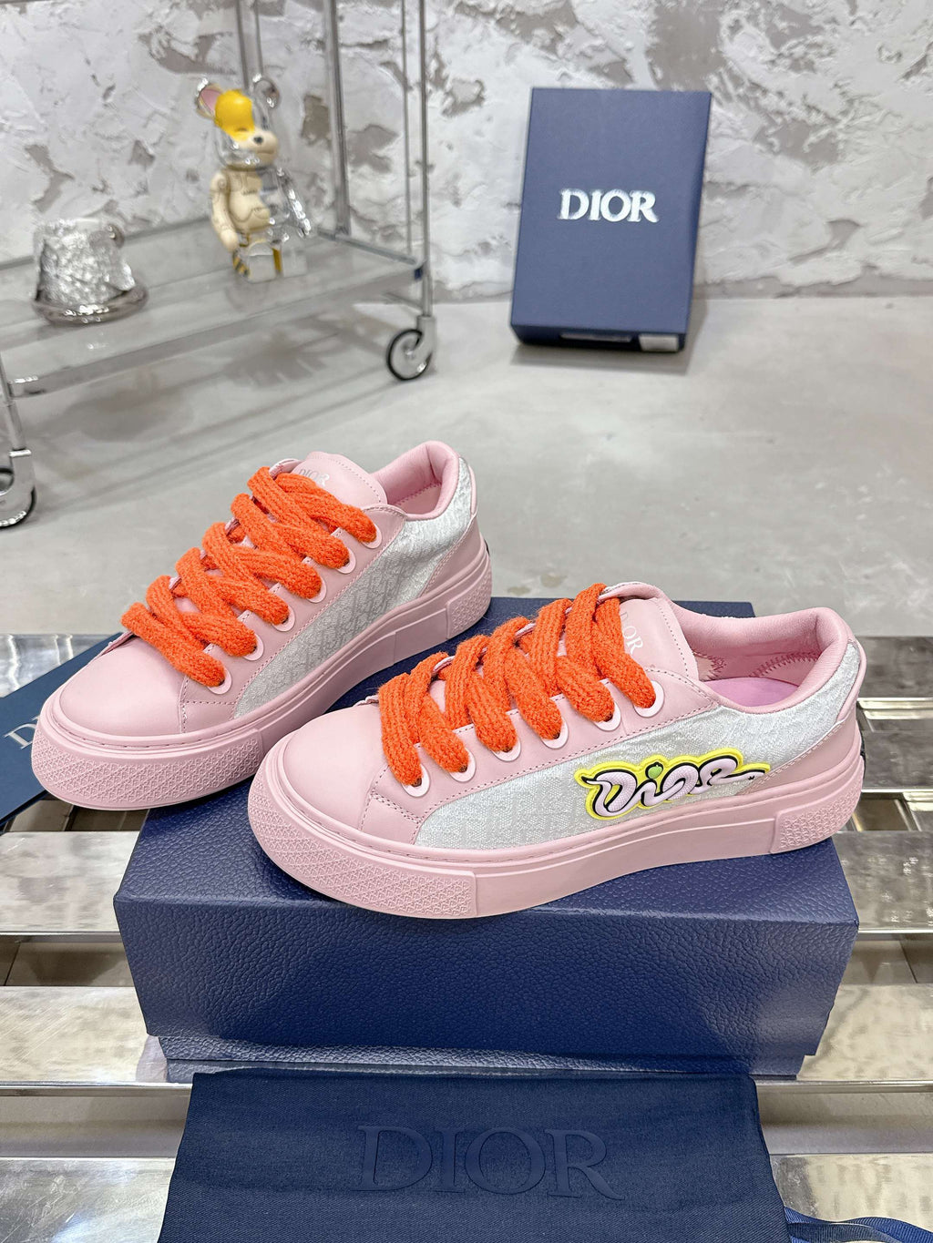 Pink and white low-top sneakers with orange laces and embroidered side logo