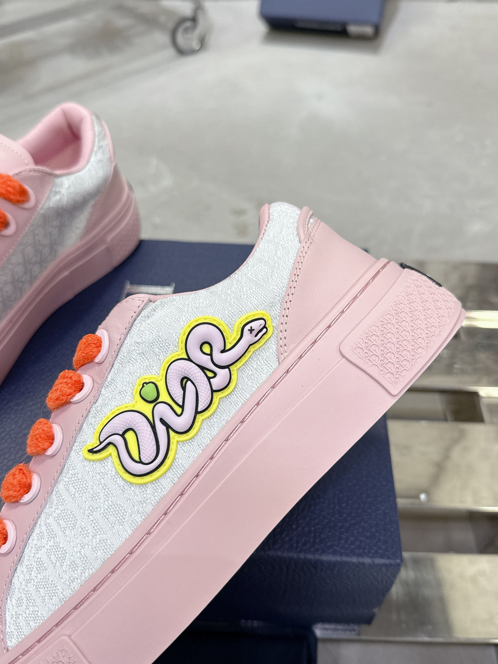 Pink and white low-top sneakers with orange laces and embroidered side lettering