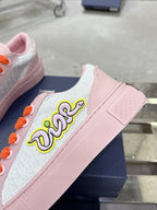 Pink and white low-top sneakers with orange laces and embroidered side lettering