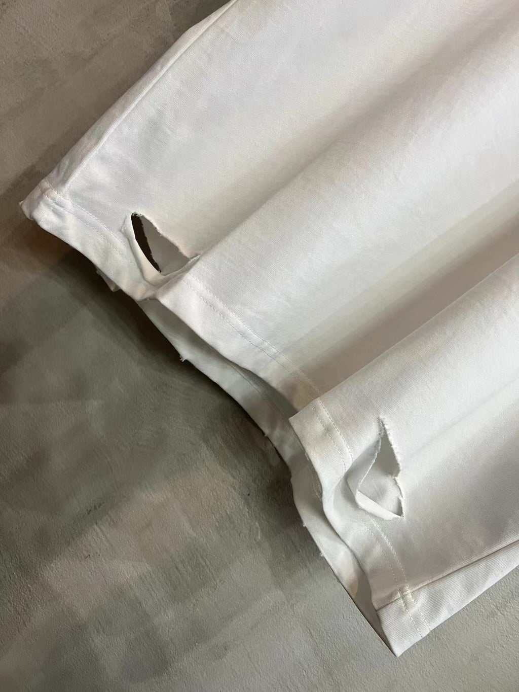 White T-shirt sleeve and side hem detail with distressed stitched opening.