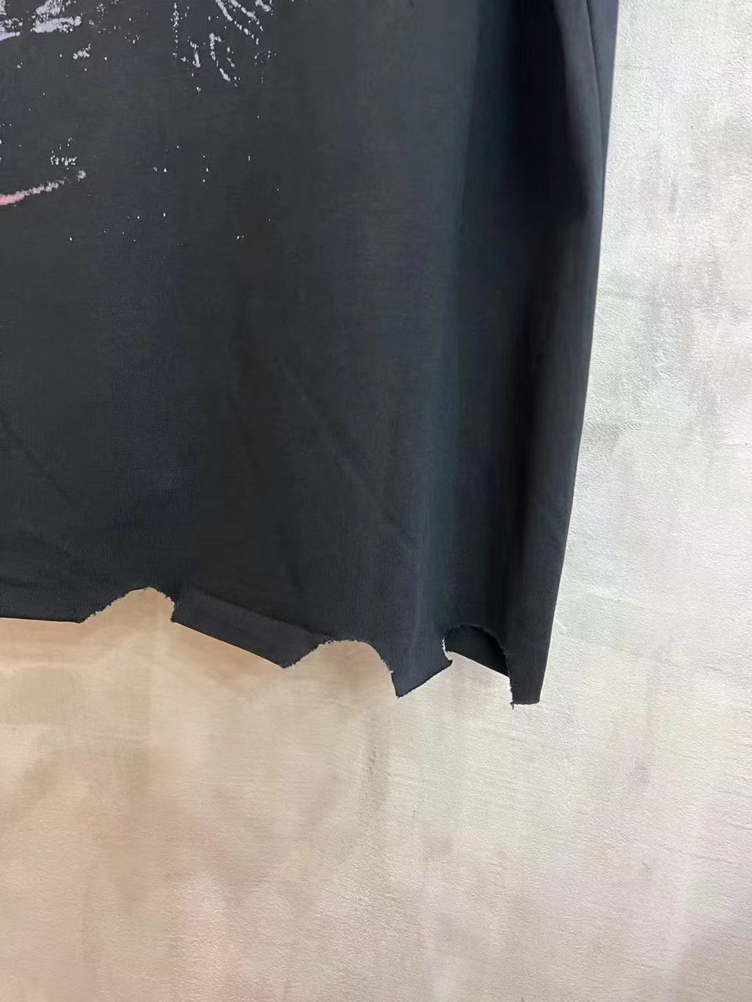 Black T-shirt bottom hem close-up with raw, uneven edges and partial neon print