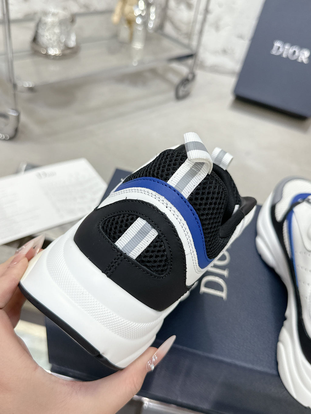 Sneaker side view with black mesh toe cap, white midsole, and blue stripe panel