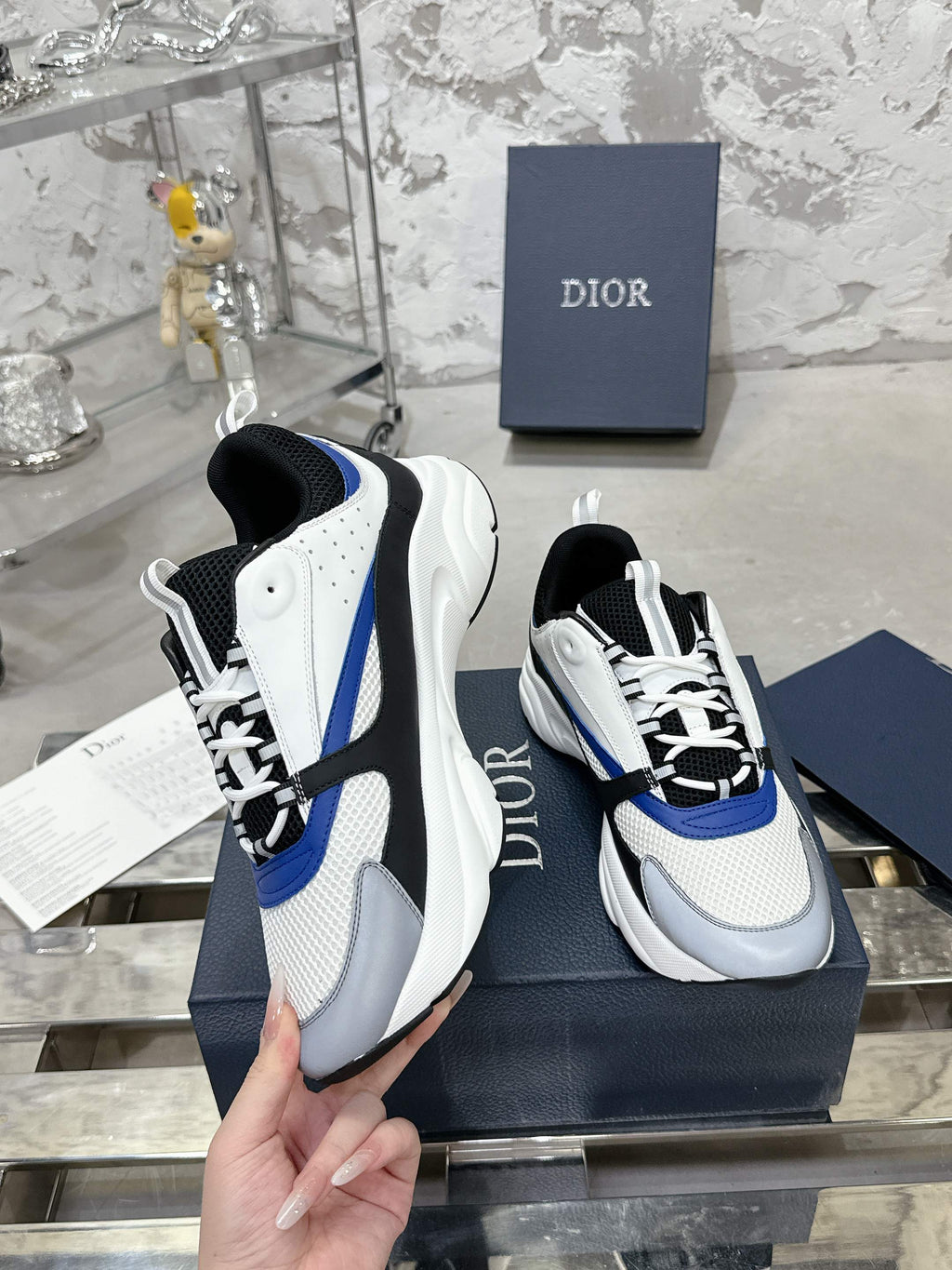 White and black low-top sneakers with blue side stripe, worn view on box
