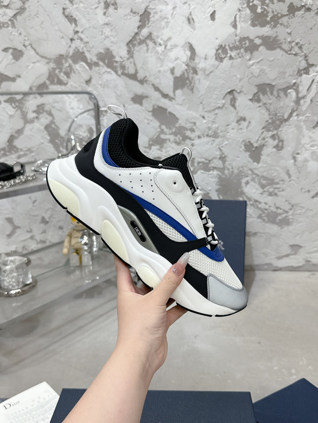 Low-top sneakers held in hand, white and black upper with blue stripe and lace-up front