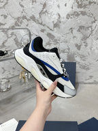 Low-top sneakers held in hand, white and black upper with blue stripe and lace-up front