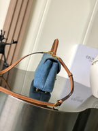 Denim top-handle bag with tan leather strap and gold-tone hardware, blue wash