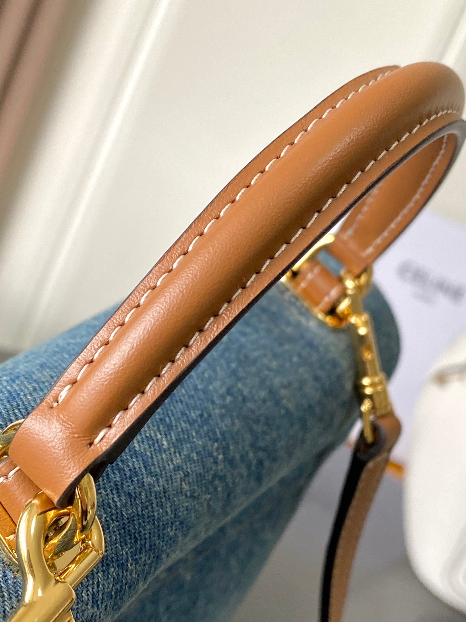 Tan leather handle close-up with visible stitching on blue denim bag