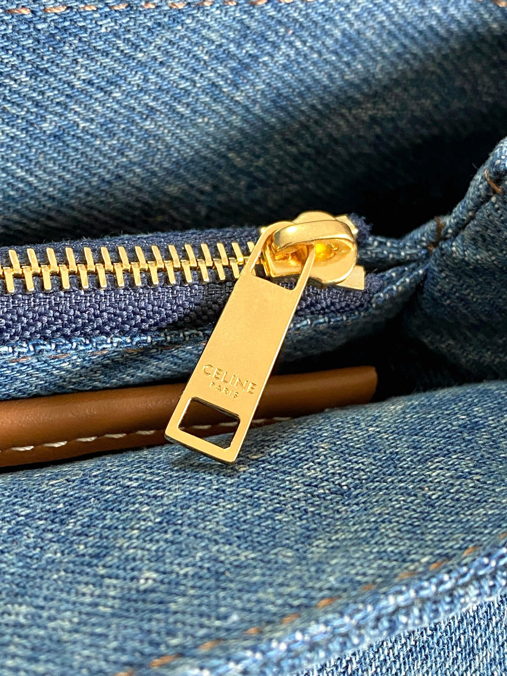 Blue denim zipper close-up with gold-tone pull and tan leather tag
