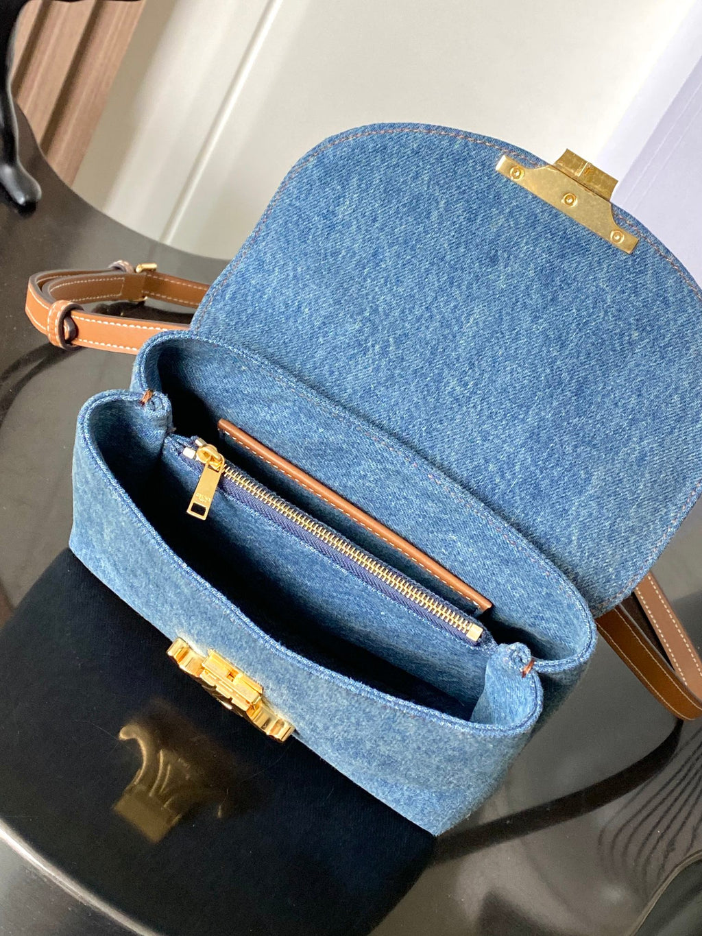 Denim flap bag open, showing zip pocket and tan leather trim, blue wash