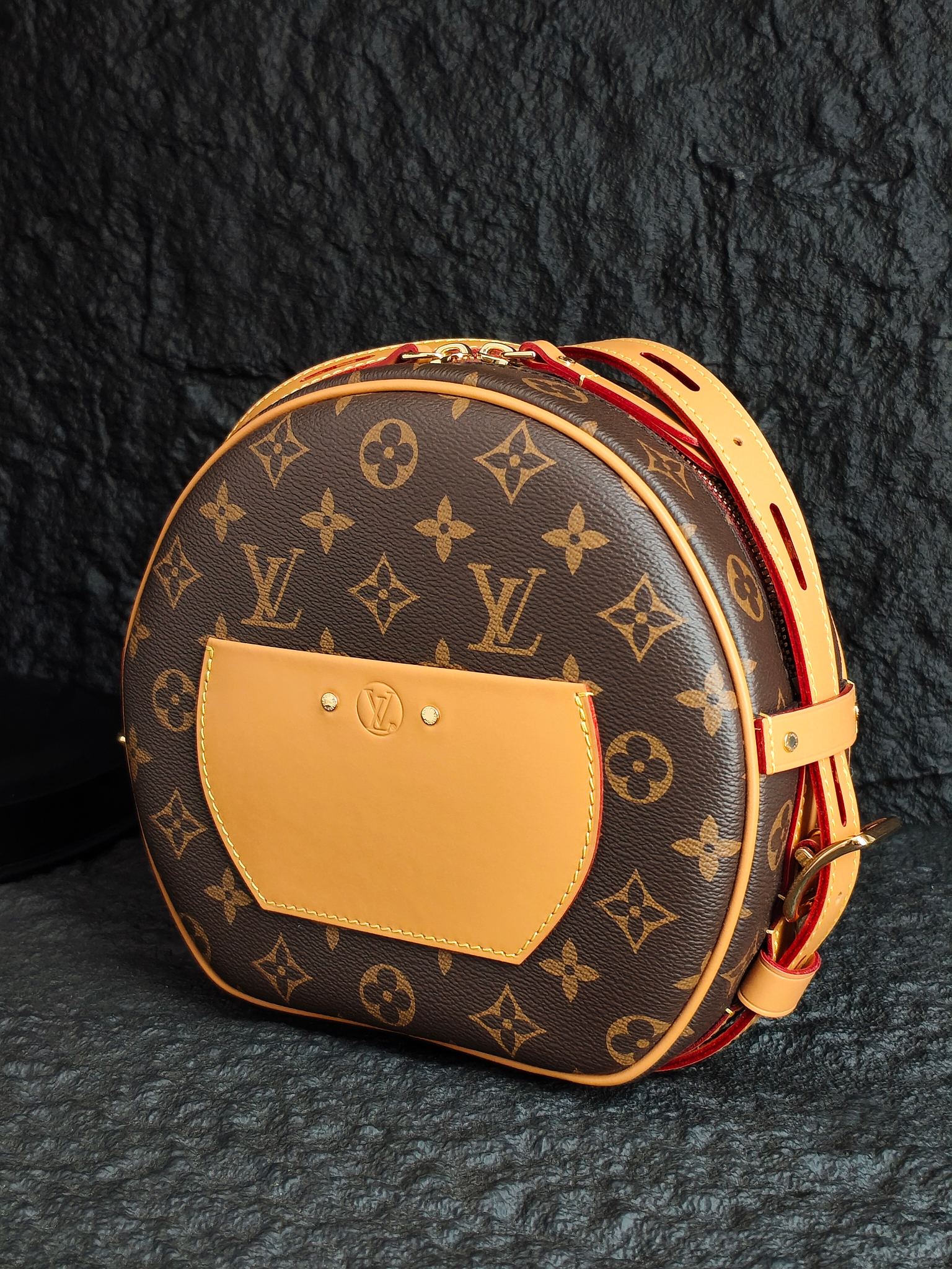 Round monogram canvas bag with tan front panel and tan strap with red zipper pull