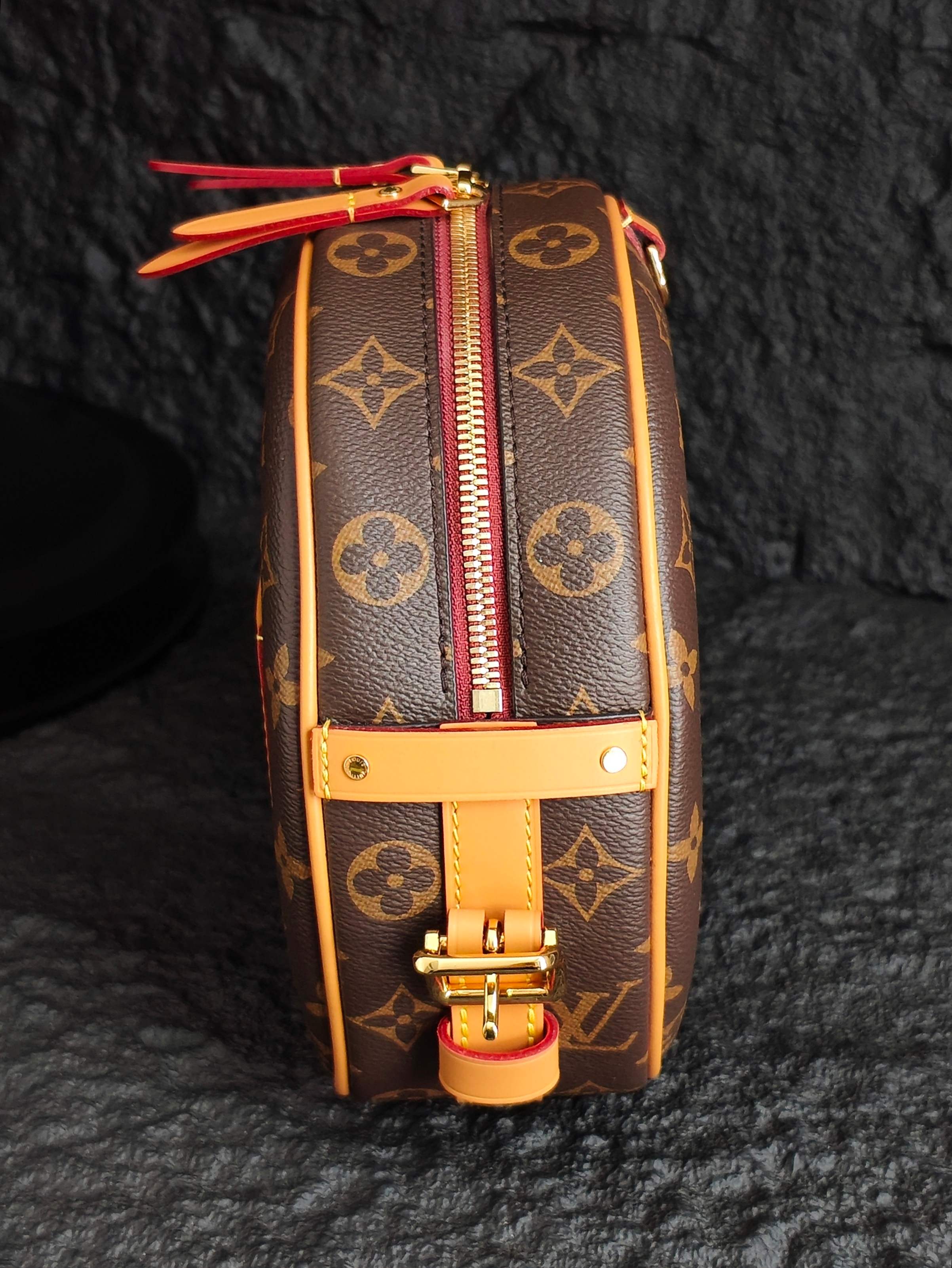 Vertical monogram canvas bag with tan leather trim, red zipper, and gold clasp