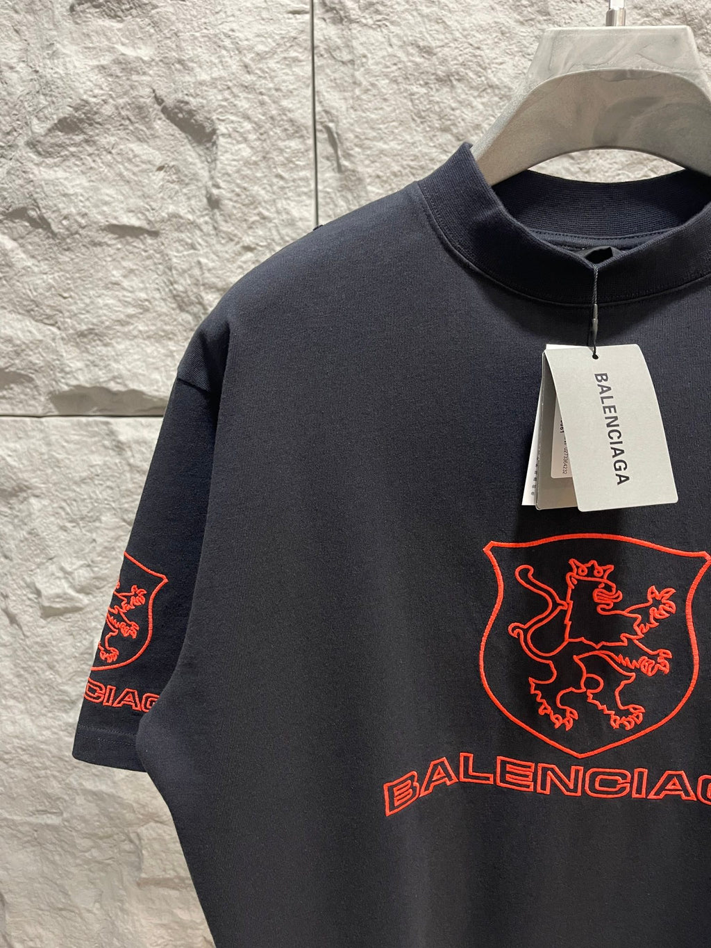 Balenciaga dark T-shirt close-up with red shield logo, crew neckline, visible Balenciaga tag