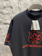 Balenciaga dark T-shirt close-up with red shield logo, crew neckline, visible Balenciaga tag