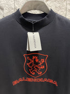 Balenciaga dark T-shirt close-up with red shield crest and Balenciaga wordmark across chest