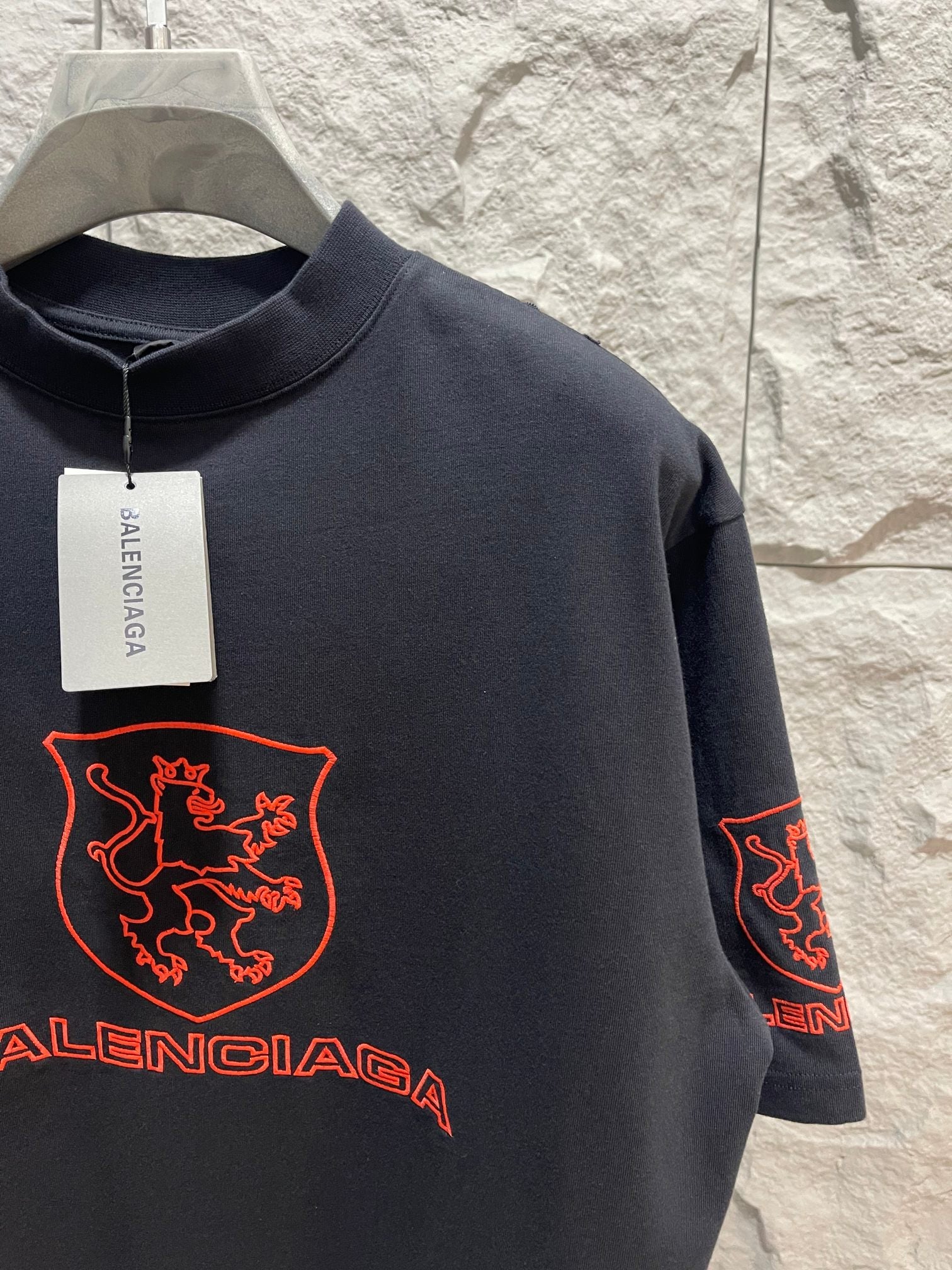 Balenciaga dark T-shirt back close-up with red shield crest and Balenciaga wordmark, tag on collar