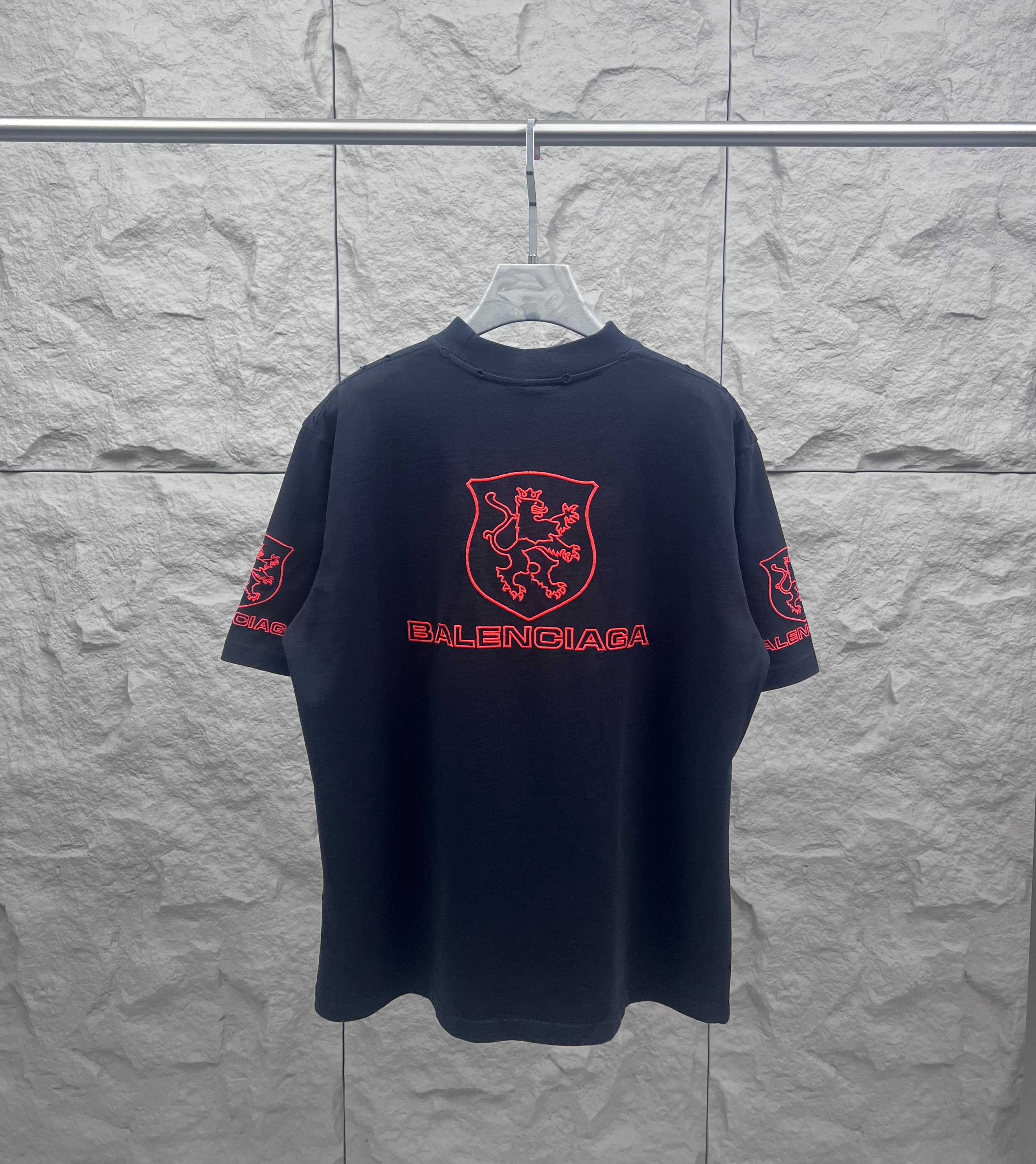 Balenciaga dark T-shirt with centered red shield crest and Balenciaga wordmark on front