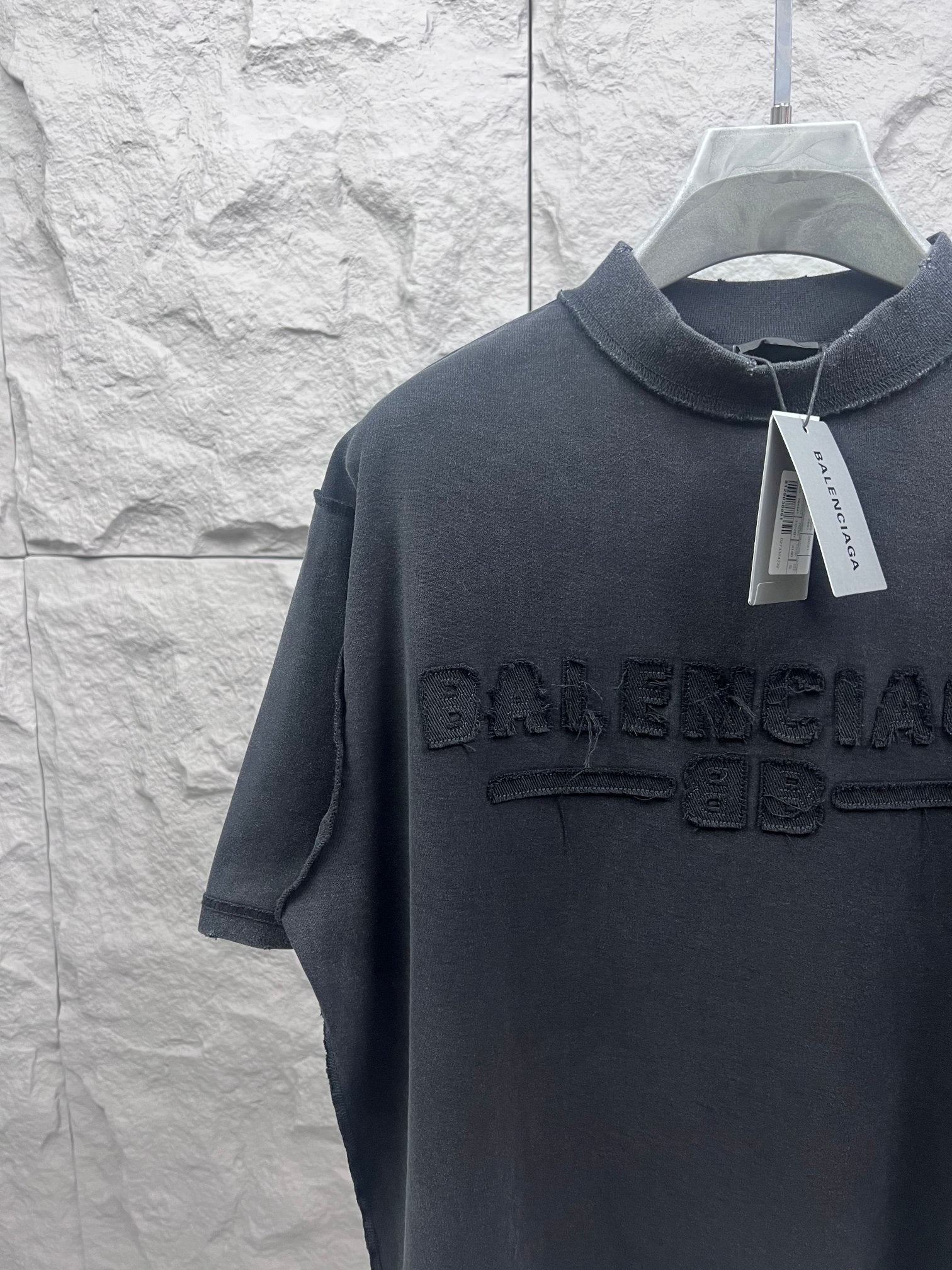Dark T-shirt close-up at chest with embossed Balenciaga logo and hanging tag