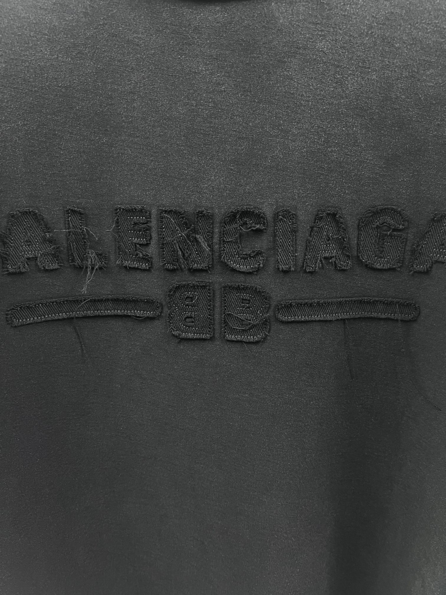 Dark T-shirt chest close-up showing embossed Balenciaga lettering and graphic