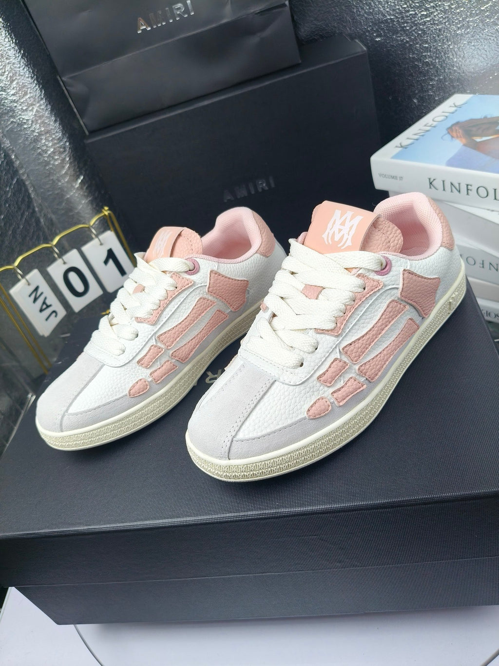 Amiri low-top sneakers in white with pink accents, lace-up, shown on display surface.