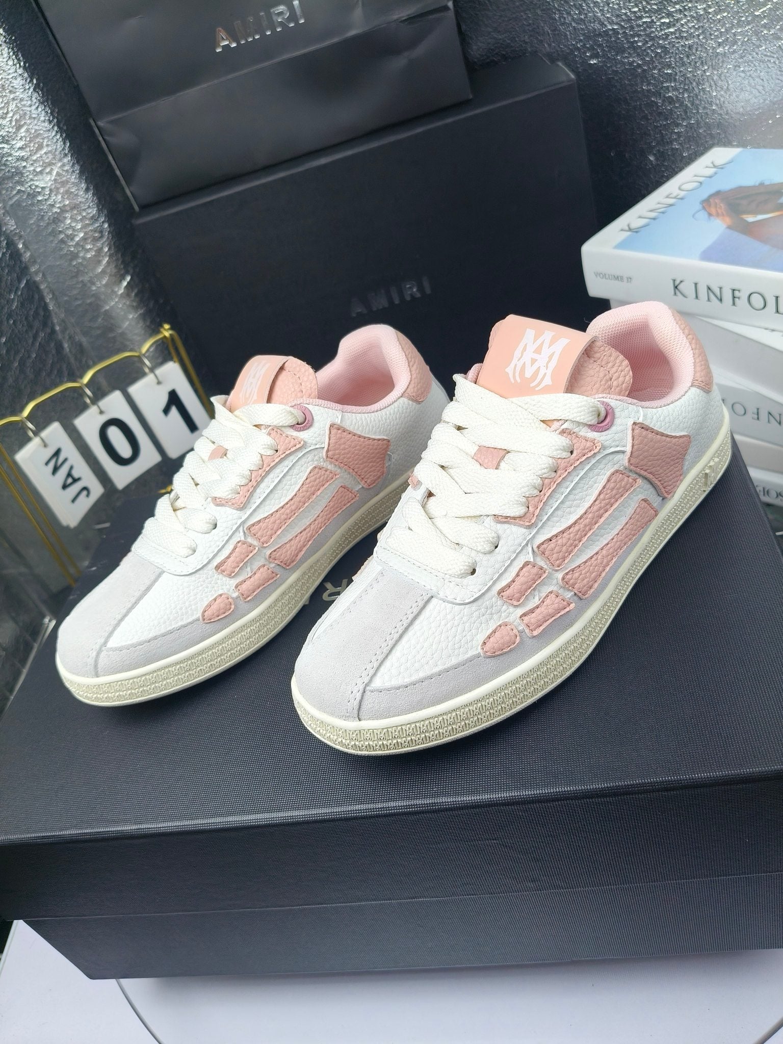 Amiri low-top sneakers in white with pink accents, lace-up, shown on display surface.