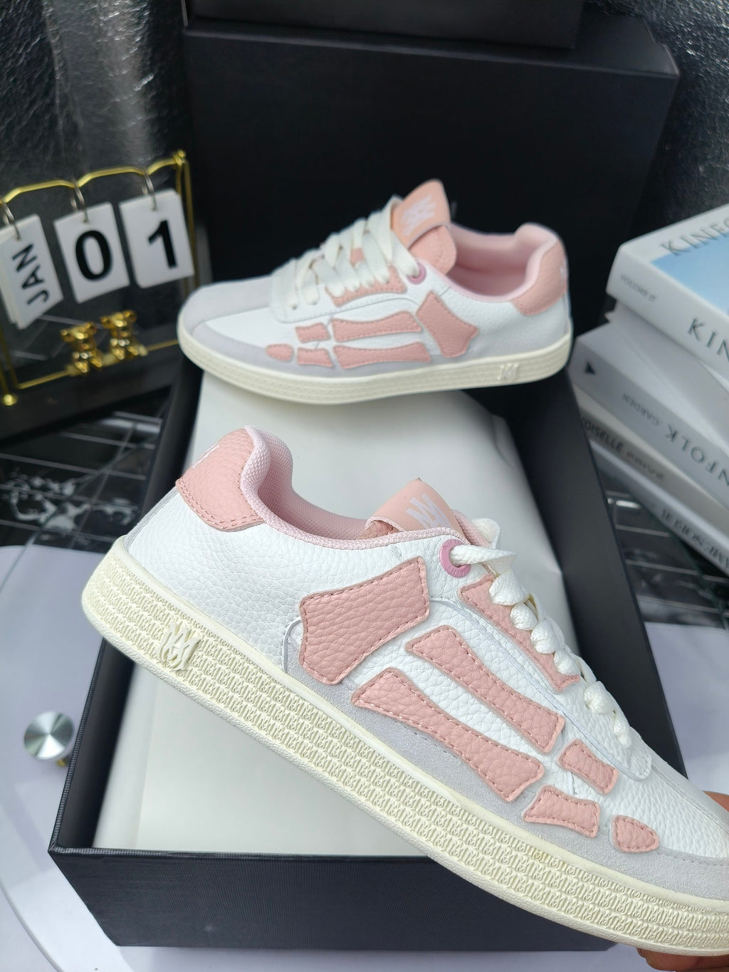 Amiri low-top sneakers in white with pink panels, lace-up, displayed on black boxes.