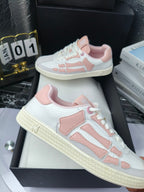 Amiri low-top sneakers in white with pink panels, lace-up, displayed on black boxes.