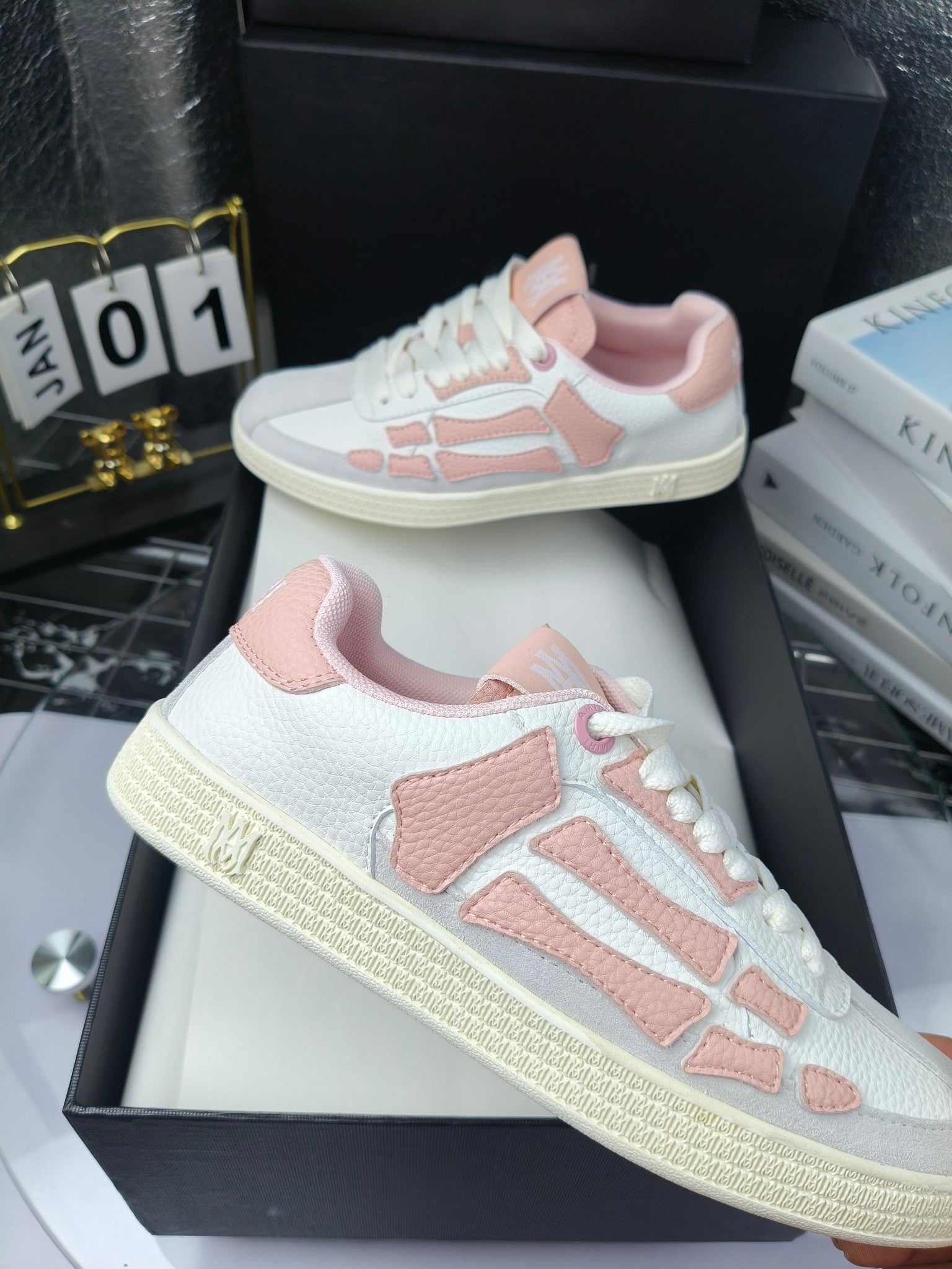 Amiri low-top sneakers in white with pink panels, lace-up, displayed on black boxes.