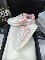 Amiri low-top sneakers with white leather look and pink accents, pair on pedestal.