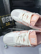 Amiri low-top sneakers close-up: white laces on upper with pink heel accent.
