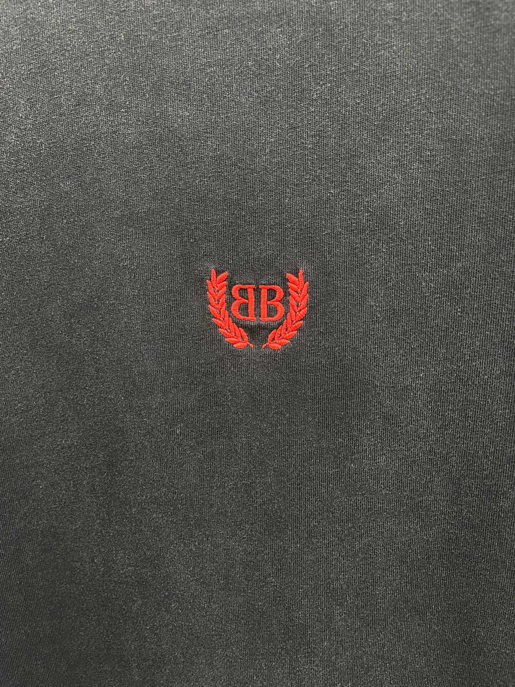 Balenciaga short-sleeve T-shirt fabric close-up, dark gray with red crest logo.