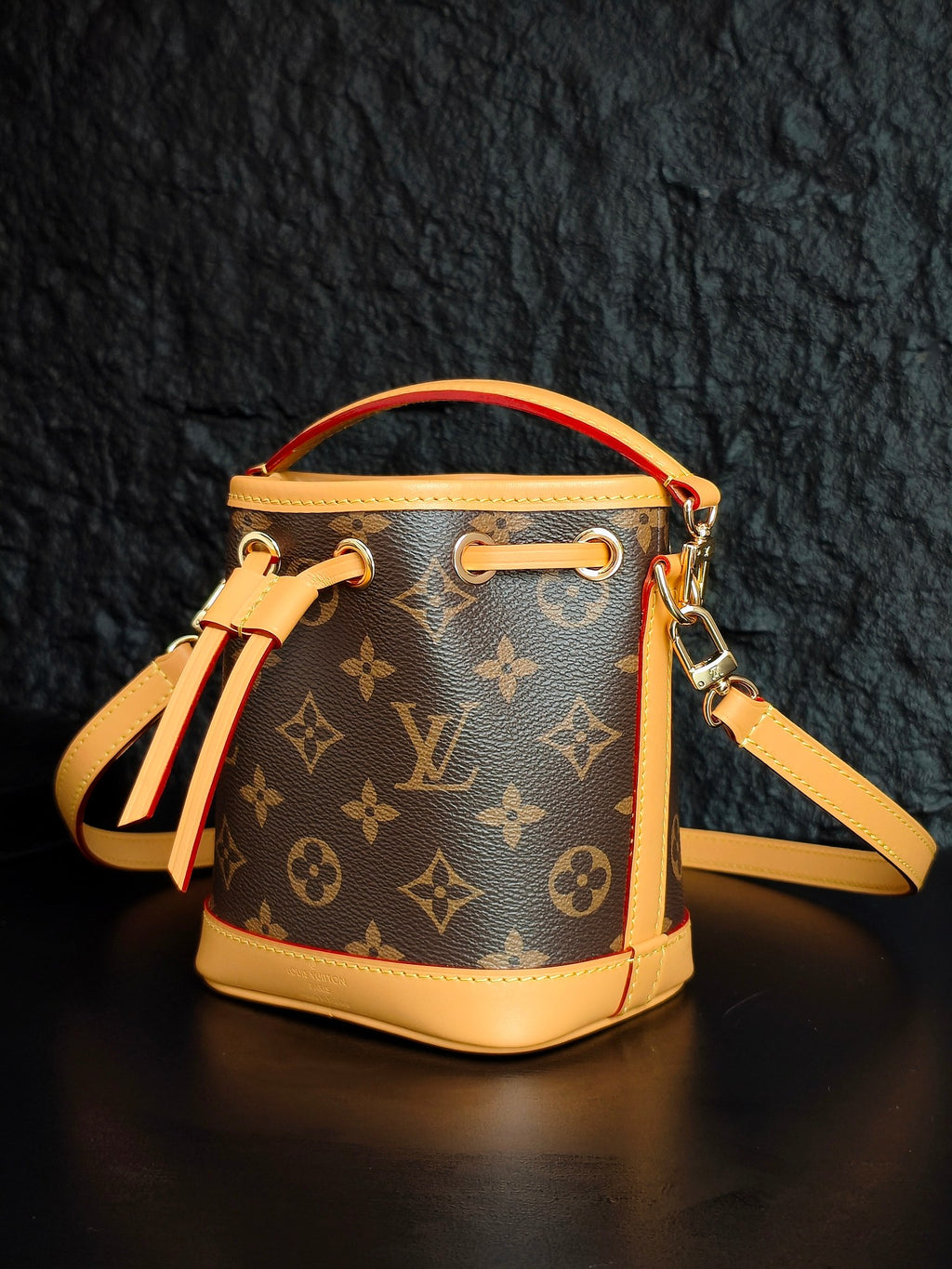 Louis Vuitton monogram bucket bag angled with crossbody strap and drawstring tassel