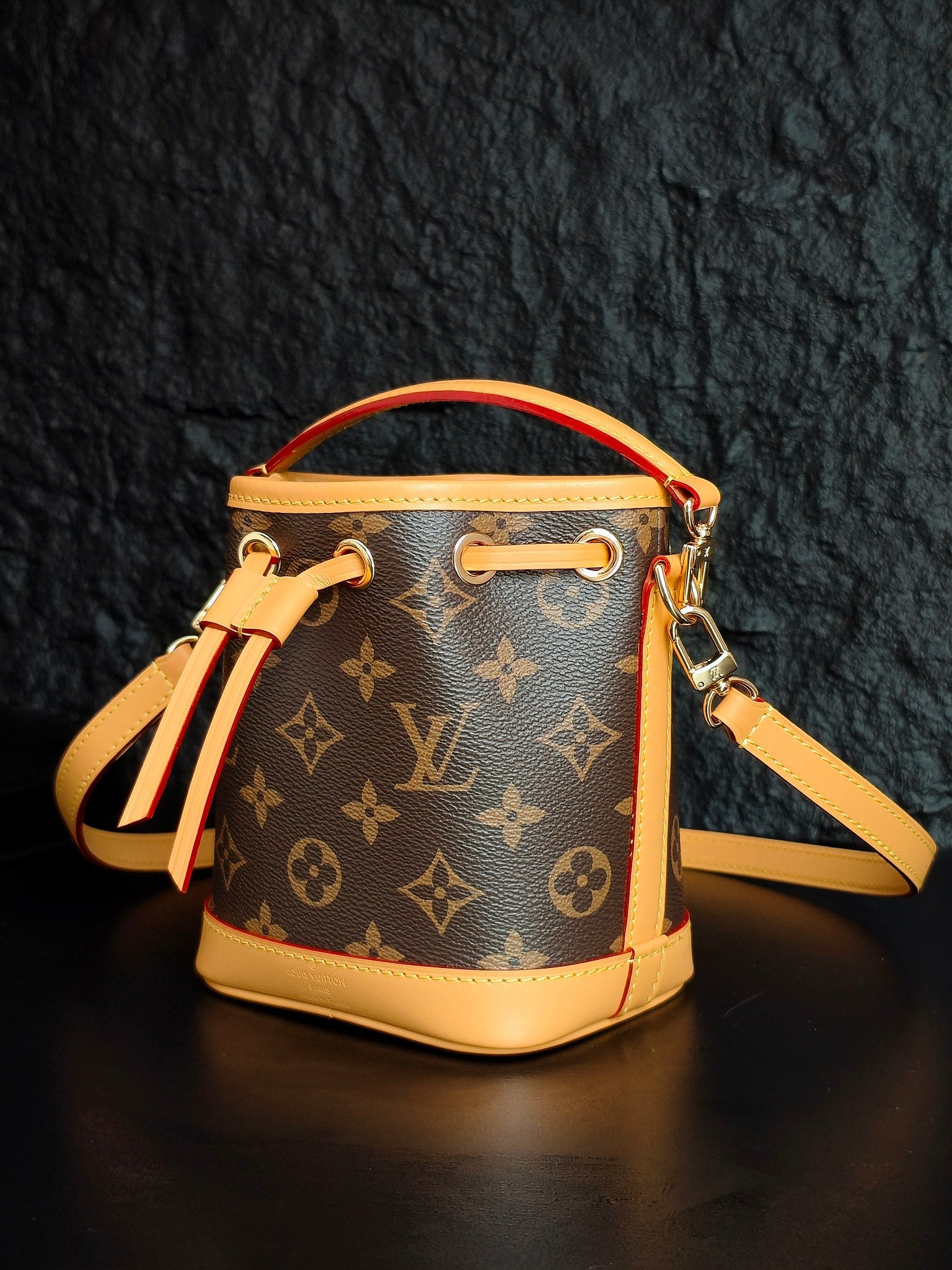 Louis Vuitton monogram bucket bag angled with crossbody strap and drawstring tassel