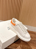 White leather low-top sneaker with orange strap accent and lace-up front