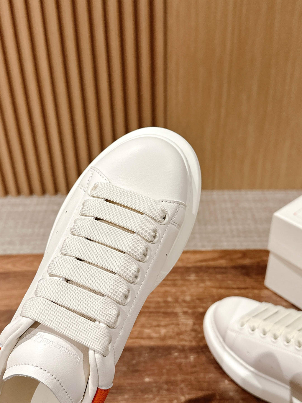 White sneaker close-up showing lace eyelets and smooth side panel with orange trim