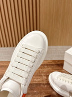 White sneaker close-up showing lace eyelets and smooth side panel with orange trim
