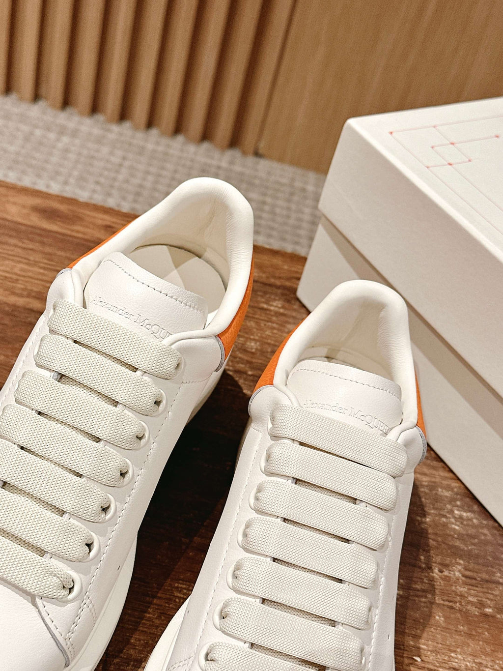 White leather sneakers with orange trim at the collar and lace-up closure